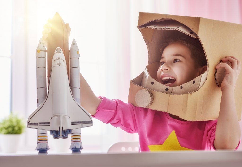 Girl playing with rocket in astronaut helmet Child in astronaut costume